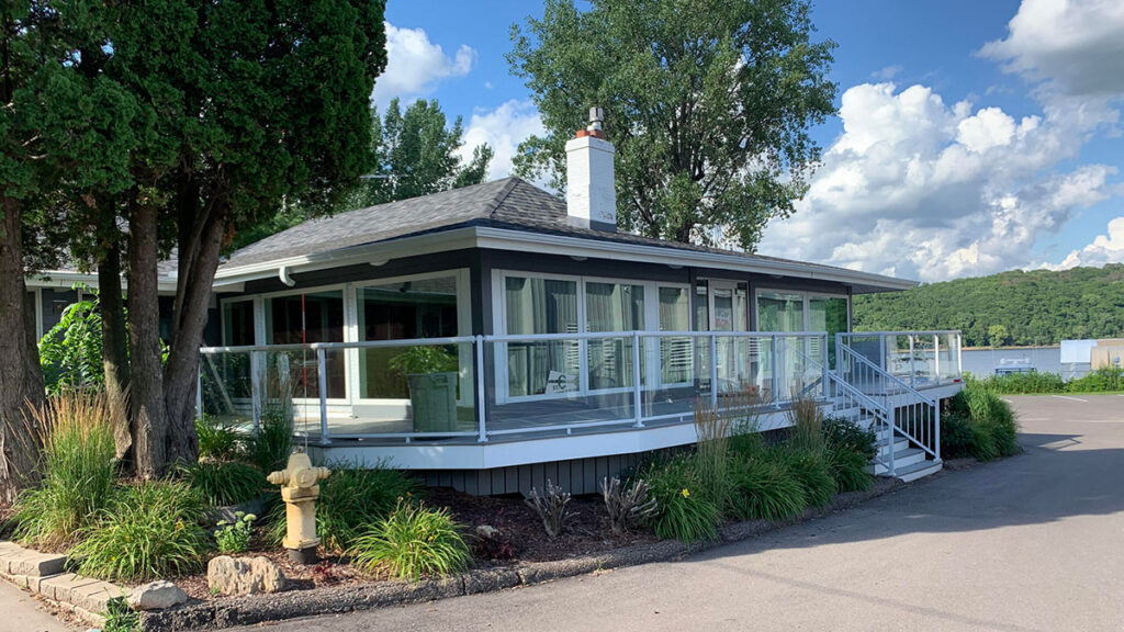 The St. Croix Yacht Club building: a dark gray building with white trim with a deck surrounding the whole building an mostly windows, providing a view of the water.