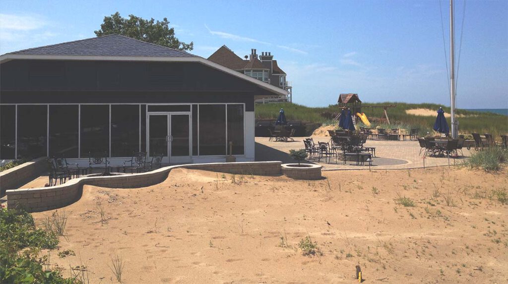 Exterior view of the Lake Michigan Yacht Club- a building with a patio with tables and chairs adjacent to a sandy beach