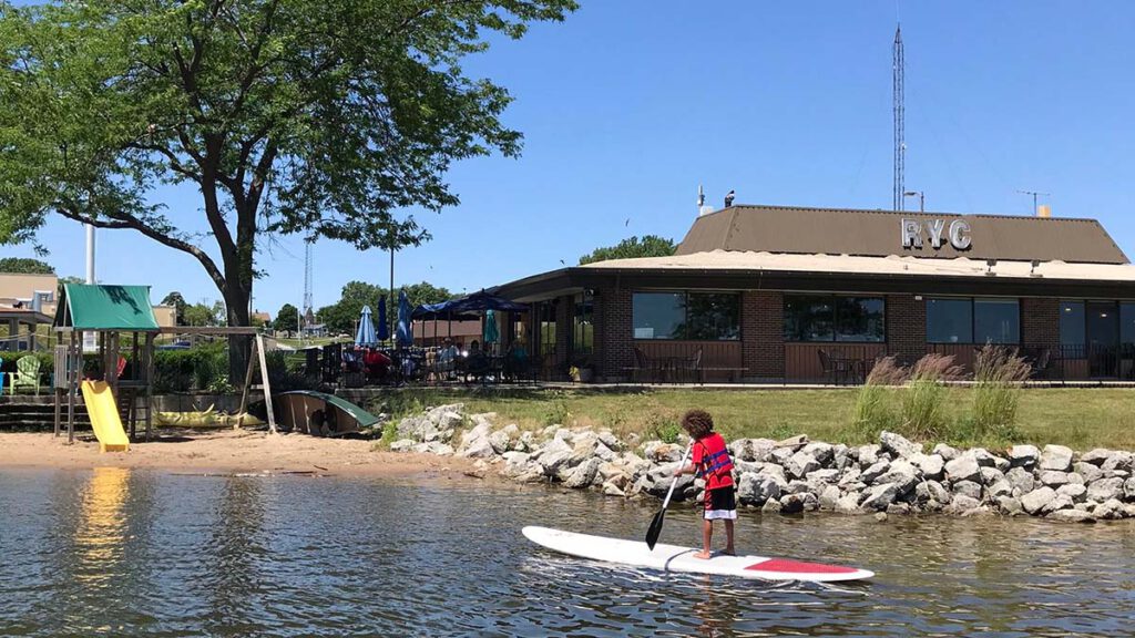 A child paddleboards in the shallow water in front of the Racine Yacht Club in Racine, Wisconsin.