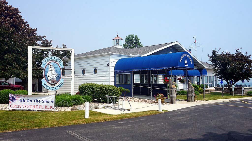 Manitowoc Yacht Club: A white building with a mini lighthouse on top and blue, half-tube shaped awnings leading in and over some windows.