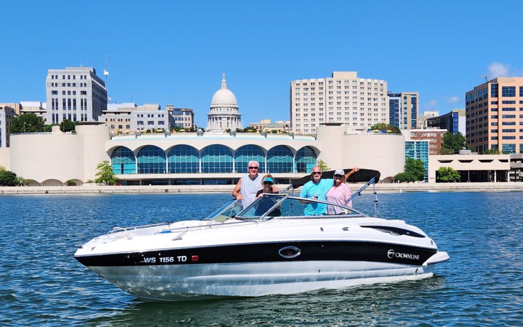 Four boaters pose for a picture in their boat on Lake Monona in Madison, Wisconsin. The state capital dome is seen in the skyline in the background.