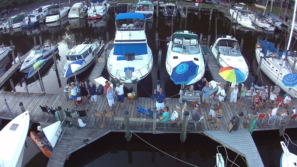 Aerial view over of the dock at the River Noir Yacht Club in South Haven, Michigan. Several boats are docked and many members of the club are on the dock amidst a celebration.